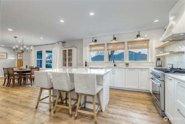 kitchen with stainless steel range, ventilation hood, a kitchen island, sink, and white cabinetry