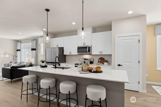 kitchen featuring sink, stainless steel appliances, pendant lighting, light hardwood / wood-style floors, and a center island with sink