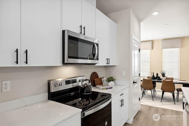 kitchen featuring white cabinetry, light stone countertops, light hardwood / wood-style floors, and appliances with stainless steel finishes