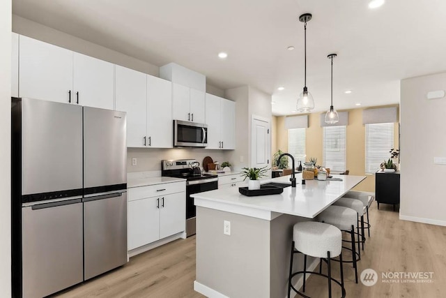 kitchen with white cabinetry, stainless steel appliances, light hardwood / wood-style floors, decorative light fixtures, and a center island with sink