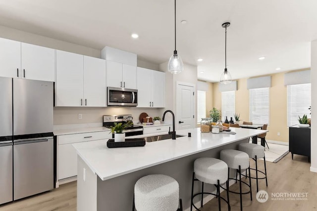 kitchen featuring light wood-type flooring, stainless steel appliances, hanging light fixtures, and a center island with sink