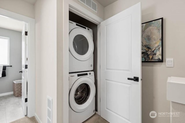 laundry area with light tile patterned floors and stacked washer and dryer