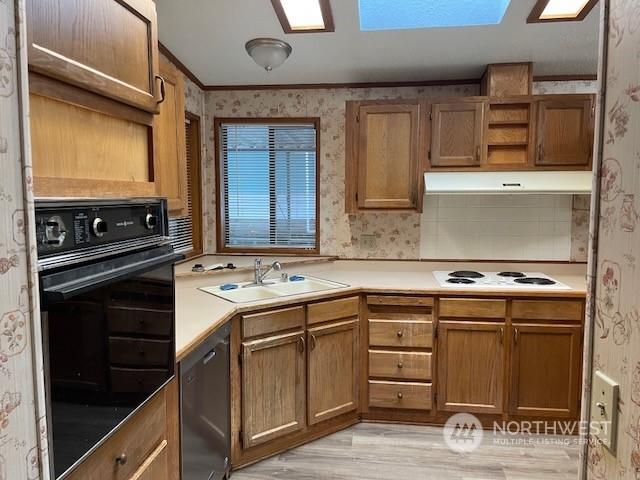 kitchen featuring black appliances, sink, light hardwood / wood-style flooring, a skylight, and ornamental molding