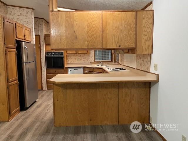 kitchen featuring light wood-type flooring, a textured ceiling, tasteful backsplash, kitchen peninsula, and stainless steel appliances