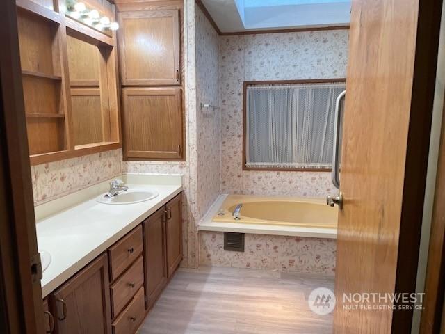 bathroom featuring wood-type flooring, vanity, a relaxing tiled tub, and a skylight