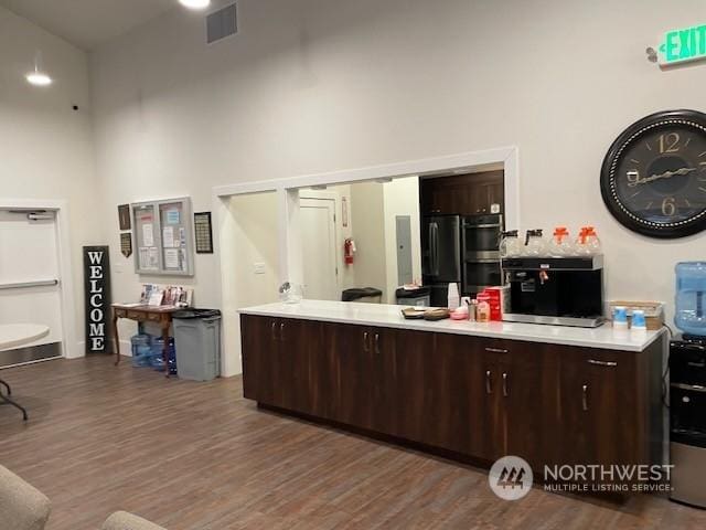 kitchen featuring dark brown cabinetry, dark wood-type flooring, and a high ceiling