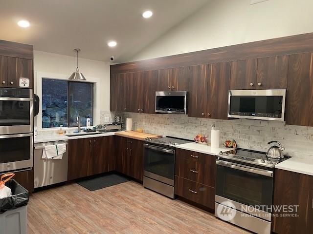 kitchen featuring tasteful backsplash, light hardwood / wood-style floors, pendant lighting, lofted ceiling, and appliances with stainless steel finishes