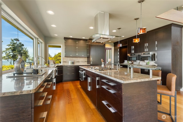 kitchen with hardwood / wood-style flooring, tasteful backsplash, decorative light fixtures, island exhaust hood, and stainless steel gas cooktop