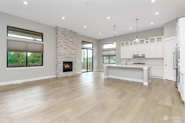 kitchen with white cabinets, hanging light fixtures, decorative backsplash, a fireplace, and an island with sink