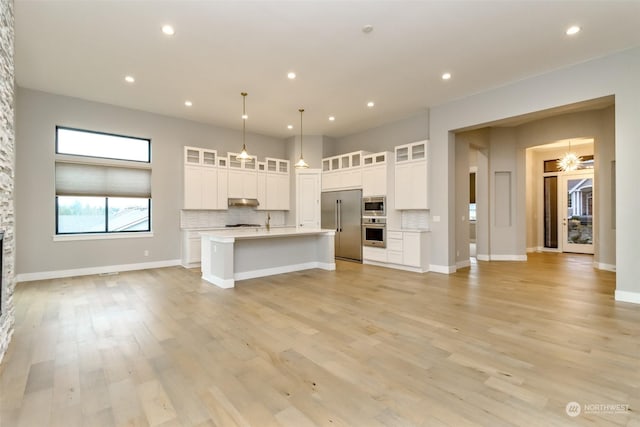 kitchen with a center island with sink, decorative backsplash, decorative light fixtures, white cabinetry, and stainless steel appliances