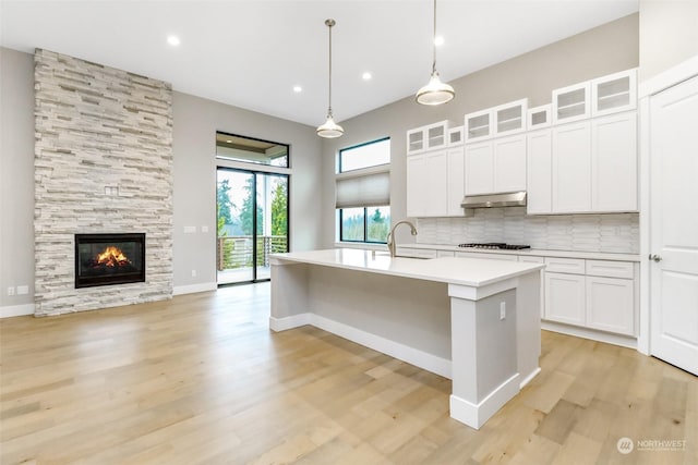 kitchen with pendant lighting, decorative backsplash, a fireplace, an island with sink, and white cabinetry