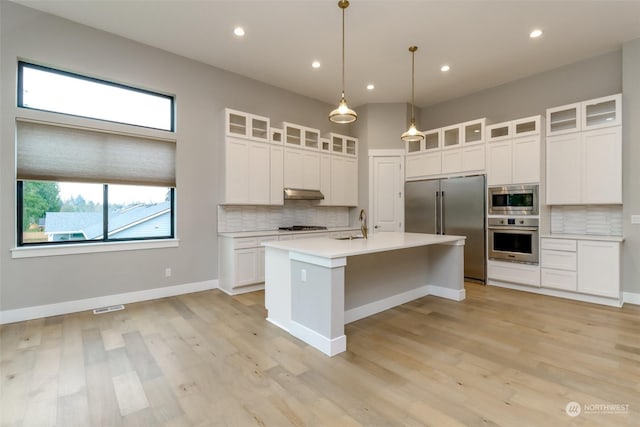 kitchen featuring built in appliances, a center island with sink, white cabinetry, and hanging light fixtures