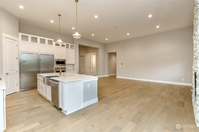 kitchen featuring appliances with stainless steel finishes, sink, pendant lighting, white cabinetry, and an island with sink