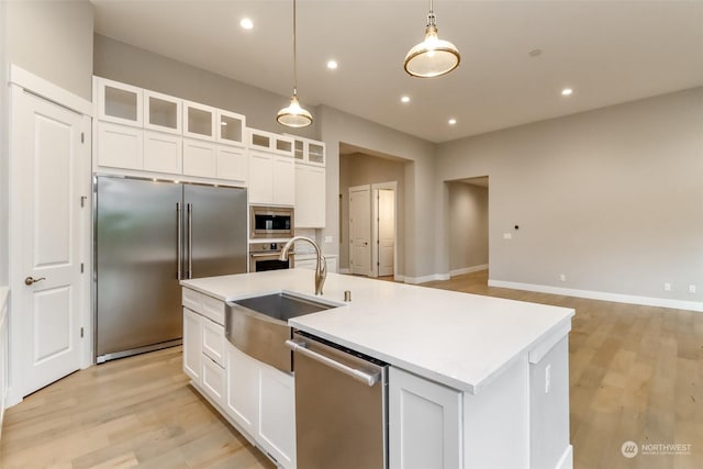 kitchen with stainless steel appliances, sink, pendant lighting, a center island with sink, and white cabinets