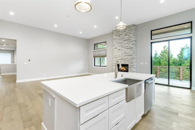 kitchen with dishwasher, a kitchen island with sink, sink, decorative light fixtures, and white cabinetry