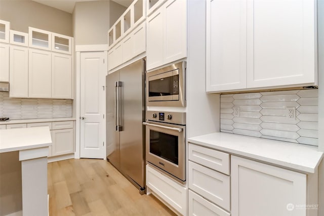 kitchen with light wood-type flooring, backsplash, stainless steel appliances, and white cabinetry