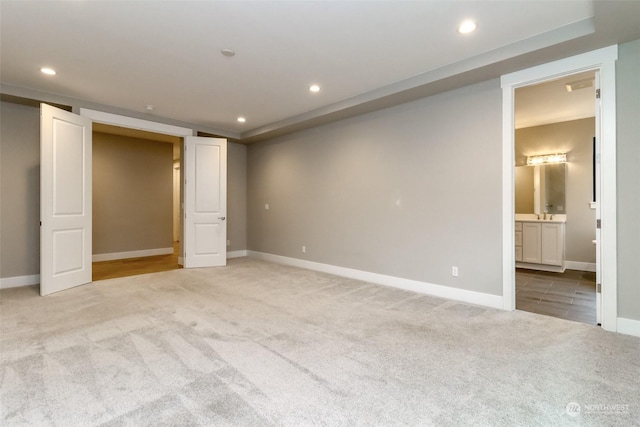 unfurnished bedroom featuring ensuite bath, light carpet, and sink