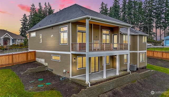 back house at dusk featuring a balcony, central air condition unit, and a patio