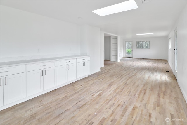 unfurnished living room featuring light hardwood / wood-style flooring and a skylight