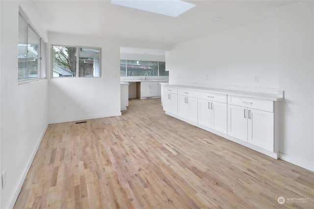 unfurnished living room with light wood-type flooring, a skylight, and sink