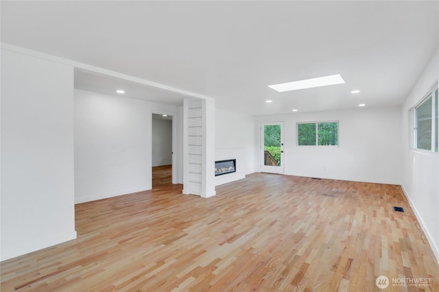 unfurnished living room featuring light wood finished floors, a skylight, plenty of natural light, a large fireplace, and recessed lighting