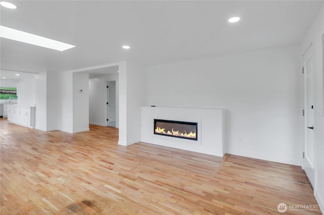 unfurnished living room featuring light wood finished floors, a glass covered fireplace, a skylight, and recessed lighting