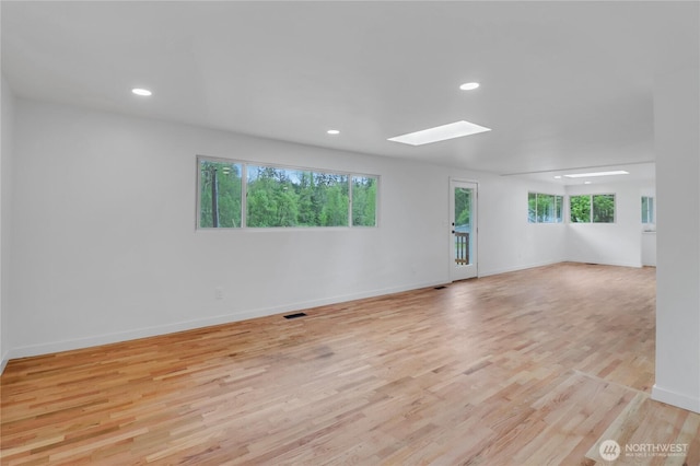 spare room with a skylight, recessed lighting, light wood-style floors, and baseboards