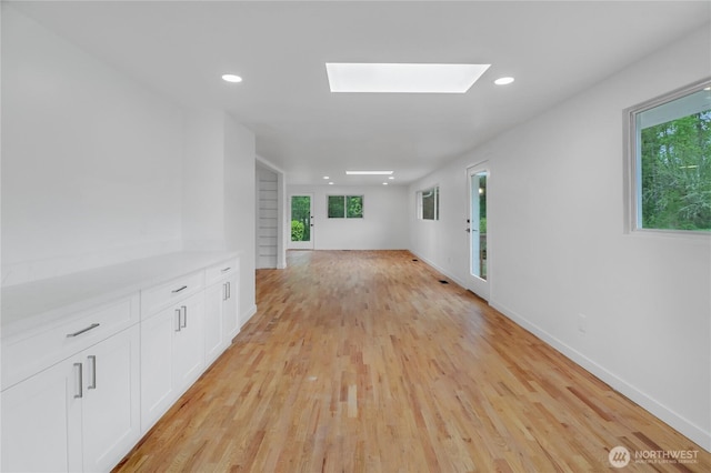 hall with light wood-style floors, plenty of natural light, a skylight, recessed lighting, and baseboards