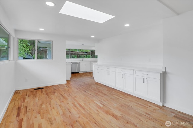 kitchen featuring a skylight, white cabinets, light countertops, light wood-style floors, and recessed lighting