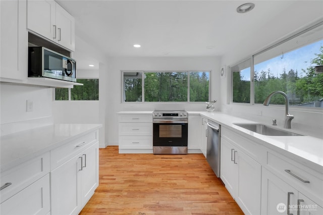 kitchen with appliances with stainless steel finishes, a sink, white cabinetry, recessed lighting, and light countertops