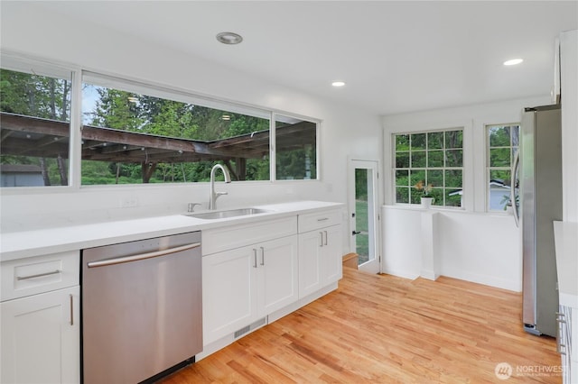 kitchen with appliances with stainless steel finishes, a sink, white cabinets, light wood-type flooring, and recessed lighting