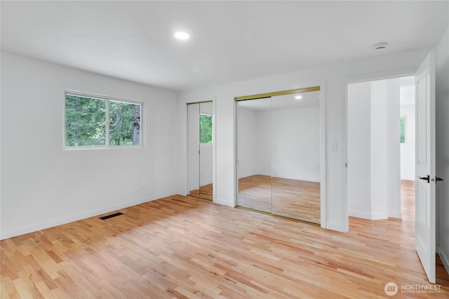 unfurnished bedroom featuring two closets, light wood-type flooring, baseboards, and recessed lighting