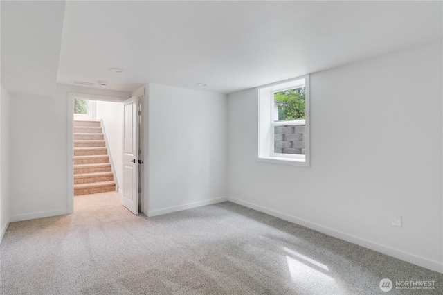 carpeted spare room featuring plenty of natural light, baseboards, and stairway