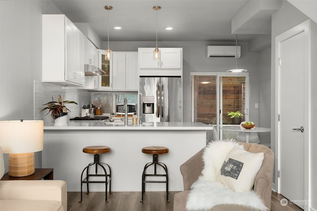 kitchen featuring an AC wall unit, white cabinets, wall chimney range hood, stainless steel fridge, and kitchen peninsula