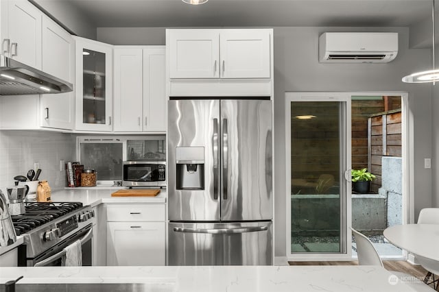 kitchen featuring white cabinetry, a wall mounted AC, appliances with stainless steel finishes, backsplash, and decorative light fixtures