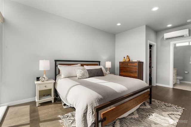 bedroom with ensuite bath, wood-type flooring, and a wall unit AC