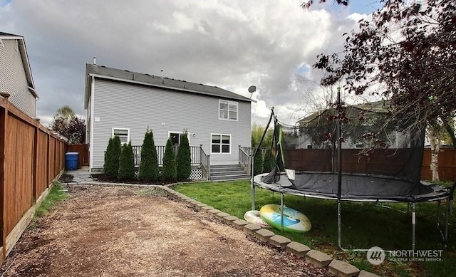 back of house featuring a trampoline, a lawn, and a wooden deck