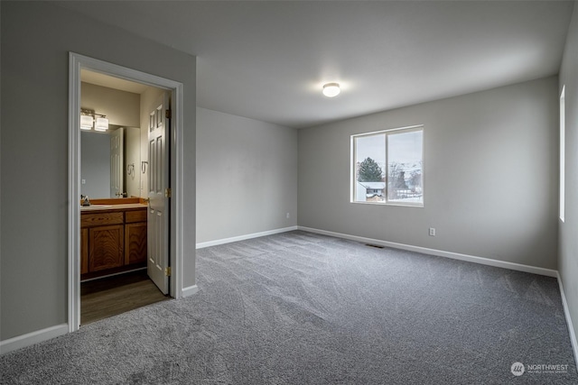 unfurnished bedroom featuring dark colored carpet and ensuite bath