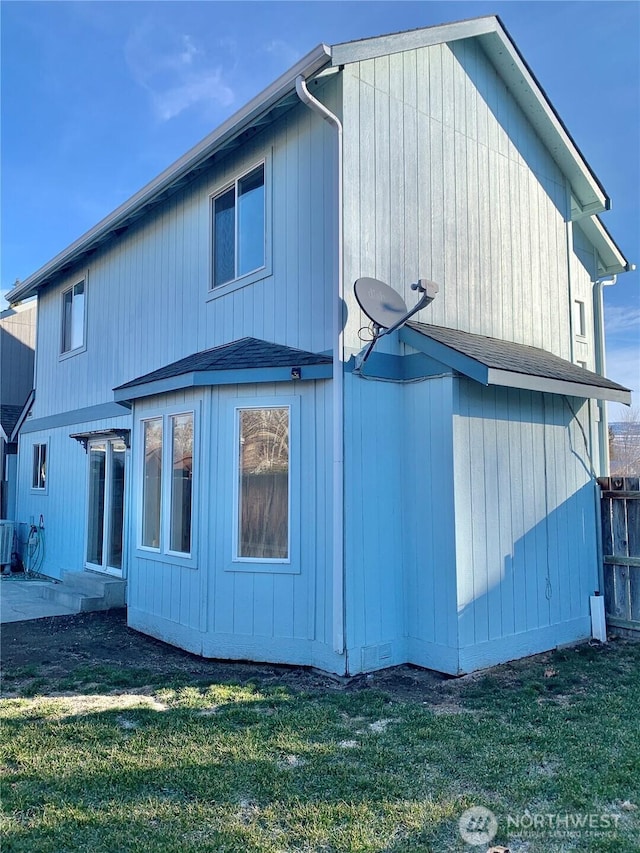 rear view of house featuring a yard, roof with shingles, and fence