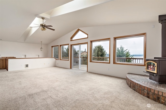 unfurnished living room featuring carpet flooring, a wood stove, ceiling fan, and lofted ceiling