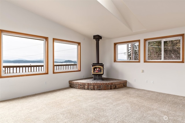 unfurnished living room with a wood stove, carpet, and vaulted ceiling