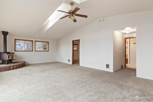 unfurnished living room with carpet flooring, a wood stove, ceiling fan, and vaulted ceiling with skylight