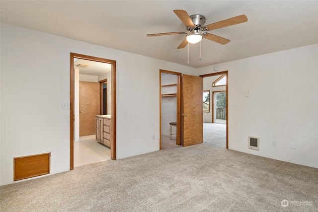 unfurnished bedroom with connected bathroom, ceiling fan, a walk in closet, light carpet, and a closet