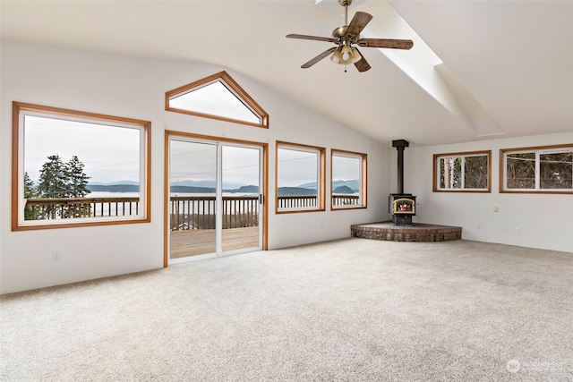 unfurnished living room with carpet floors, a wood stove, ceiling fan, and vaulted ceiling