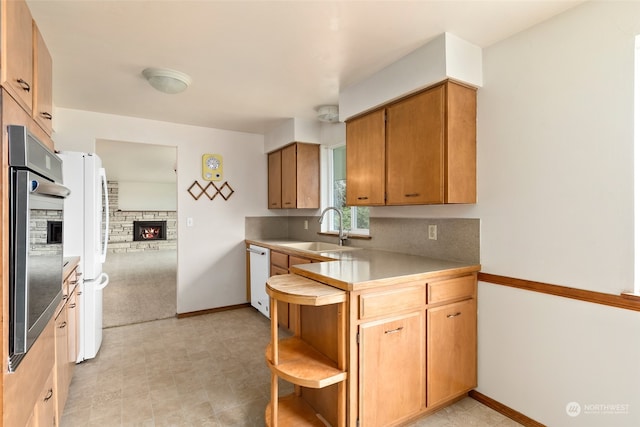 kitchen with kitchen peninsula, a stone fireplace, white appliances, and sink