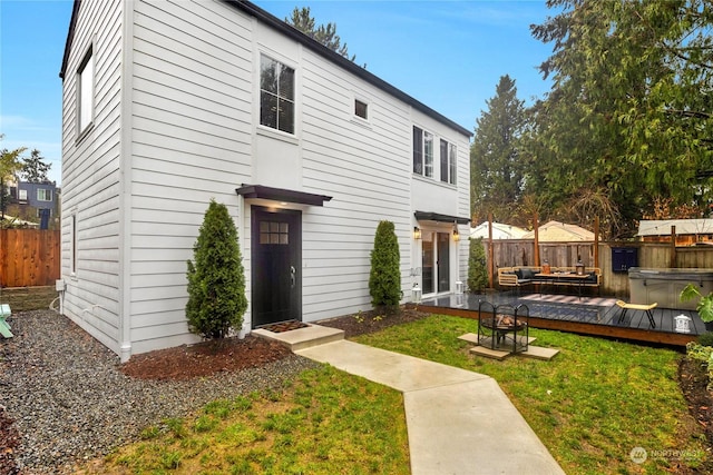 view of front of home featuring a hot tub, a front lawn, a deck, and an outdoor living space with a fire pit