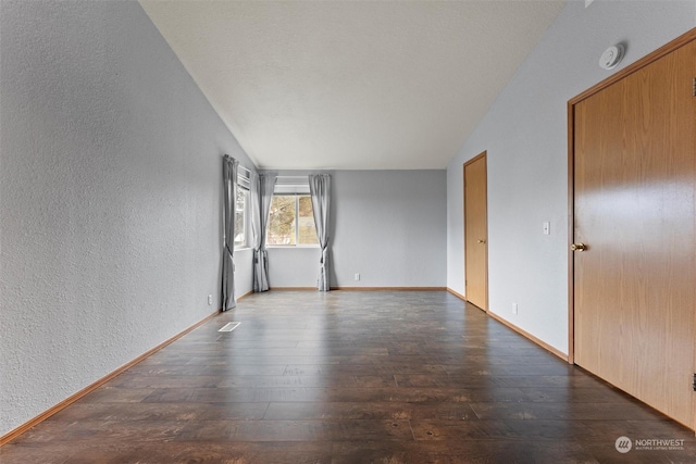 empty room with dark hardwood / wood-style flooring and vaulted ceiling