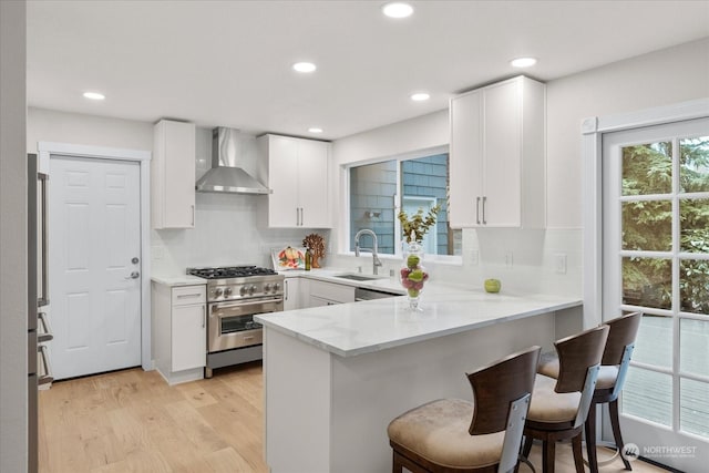 kitchen featuring sink, high end stove, white cabinetry, and wall chimney range hood