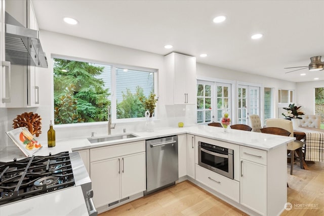 kitchen with kitchen peninsula, appliances with stainless steel finishes, light wood-type flooring, sink, and white cabinetry