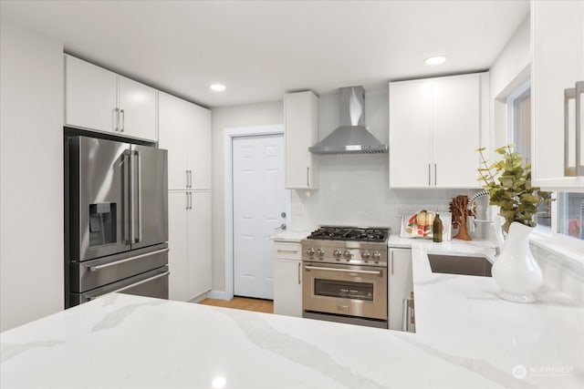 kitchen featuring white cabinets, high end appliances, and wall chimney exhaust hood